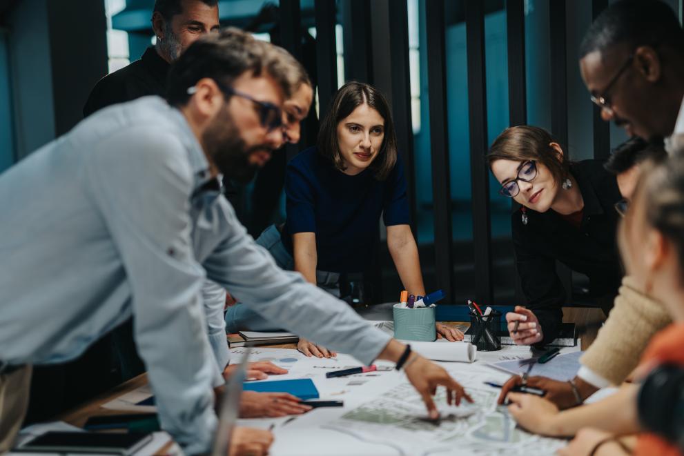 A diverse group of multigenerational business people collaborates on a project. They engage in innovative thinking and teamwork, highlighting creativity and cooperative strategies in a modern office.