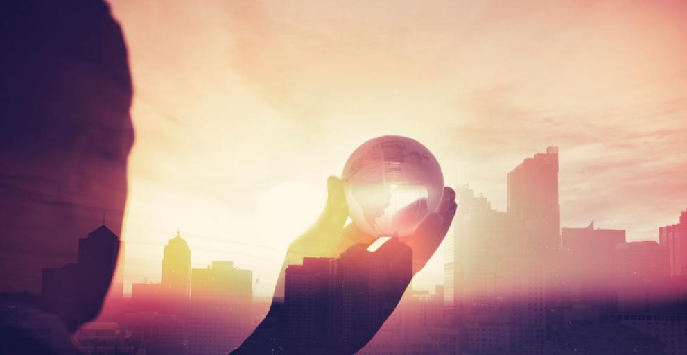 Business man in suit with cityscape montage. Business man in suit with cityscape montage. The man is unrecognizable and you cannot see his face. He is superimposed onto a city skyline at sunset. He is holding a world map globe like a crystal ball. 